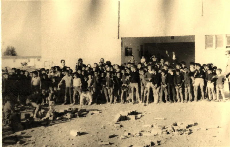 Fotografía antigua en tonos sepia de un grupo numeroso de niños sobre un solar de tierra