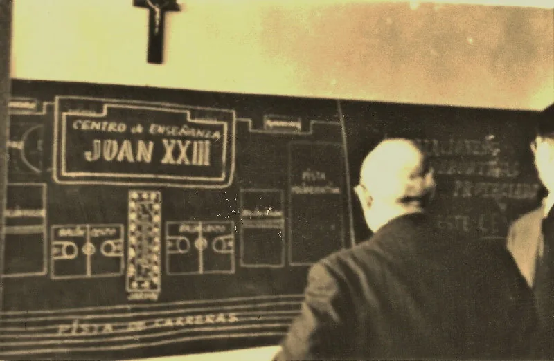 Fotografía antigua de un hombre de espaldas ante una pizarra con el rótulo Juan XXIII y un plano