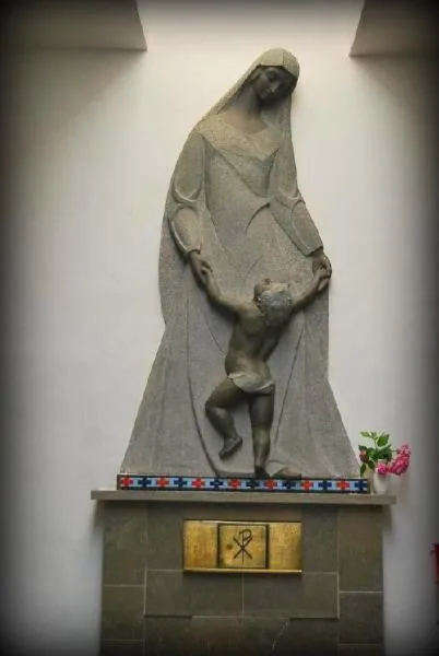 Escultura de piedra de una madre con un niño, sobre un pedestal con flores